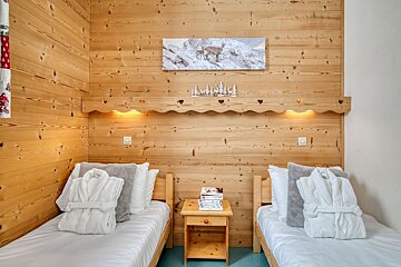 A cozy wooden chalet bedroom featuring two single beds with folded white bathrobes and a central nightstand.