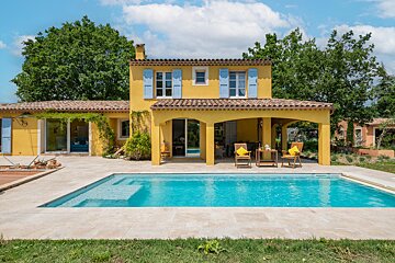 A yellow house with blue shutters sits next to a large swimming pool
