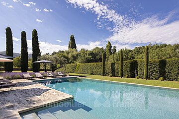 A large swimming pool is surrounded by lawn chairs and umbrellas and is for sale by immobilier frank