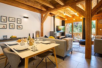 Cozy alpine chalet interior featuring a set dining table, a living area with a fireplace, and exposed wooden beams.