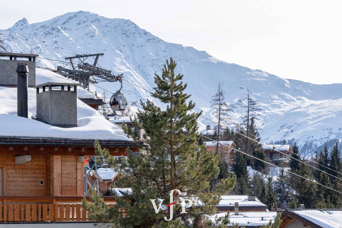 Snow-covered wooden chalets and a gondola lift set against a backdrop of majestic, snow-capped mountains.