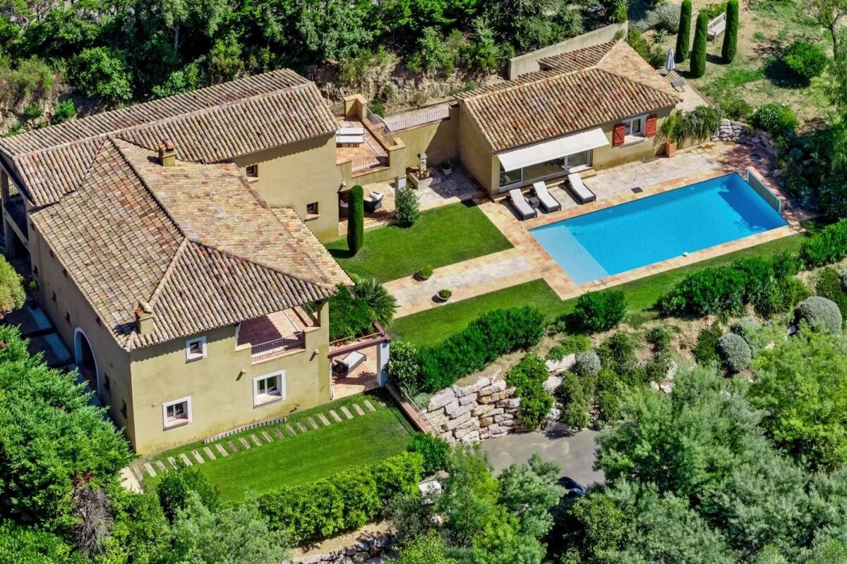 Aerial view of a sprawling Mediterranean villa with red-tiled roofs, a large blue swimming pool, manicured lawns, and lush green landscaping.