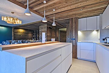 A chic modern kitchen with white cabinets and island contrasts with rustic wooden ceilings and walls, opening to a cozy dining area.