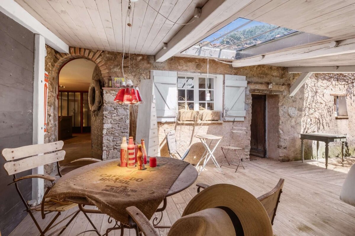 A charming rustic covered patio featuring stone walls, wooden beams, a coffee-sack covered table with drinks, and a skylight.