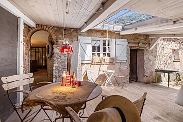 A charming rustic covered patio featuring stone walls, wooden beams, a coffee-sack covered table with drinks, and a skylight.