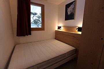 A cozy bedroom with a single bed, illuminated wooden headboard, leopard art, and a window framing a snowy outdoor scene.