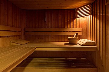 Interior of a wooden sauna room with warm lighting, multi-level benches, and a traditional bucket with a ladle.