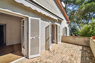 A balcony with white shutters and trees in the background