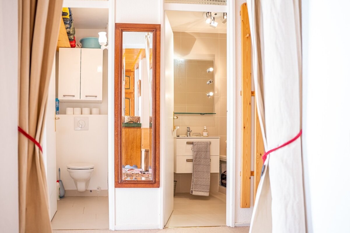 A split bathroom layout with a toilet room on the left and a sink vanity on the right, separated by a long wooden-framed mirror.