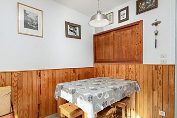 A rustic dining nook with wood-paneled walls, framed art, a table with a heart-patterned tablecloth, and wooden stools.