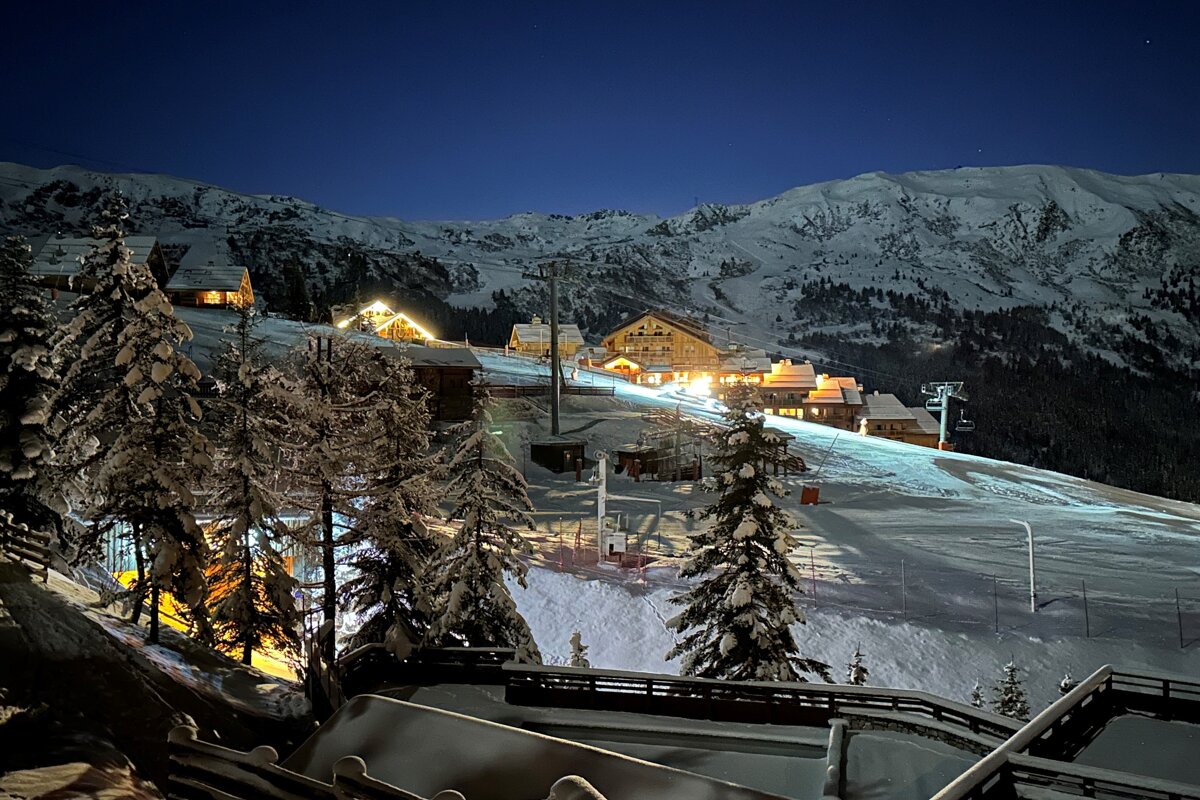 A ski resort is lit up at night with mountains in the background