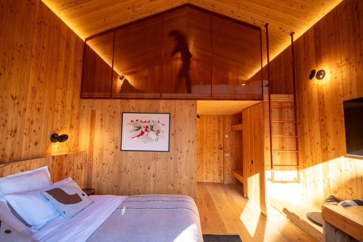 Cozy wood-paneled cabin bedroom with a bed in the foreground and a loft area above featuring the silhouette of a person.
