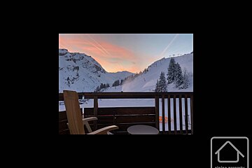 A chair on a balcony overlooking a snowy mountain range