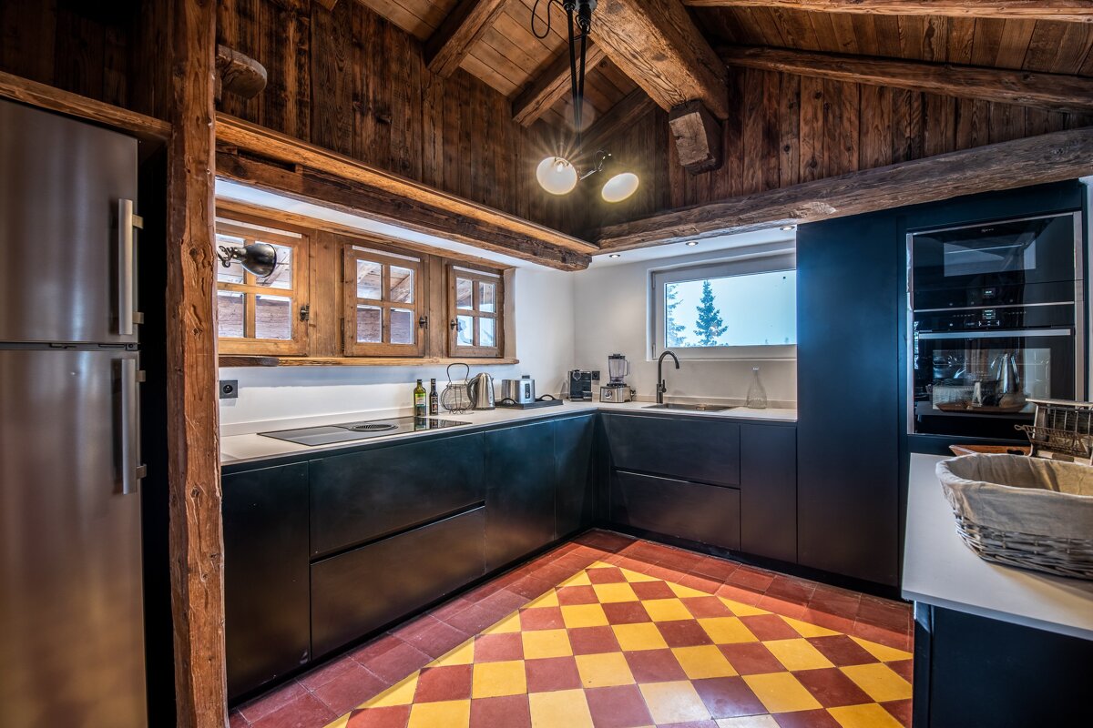 A rustic cabin kitchen featuring modern black cabinets, wooden beams, and a bold yellow and red checkered floor.