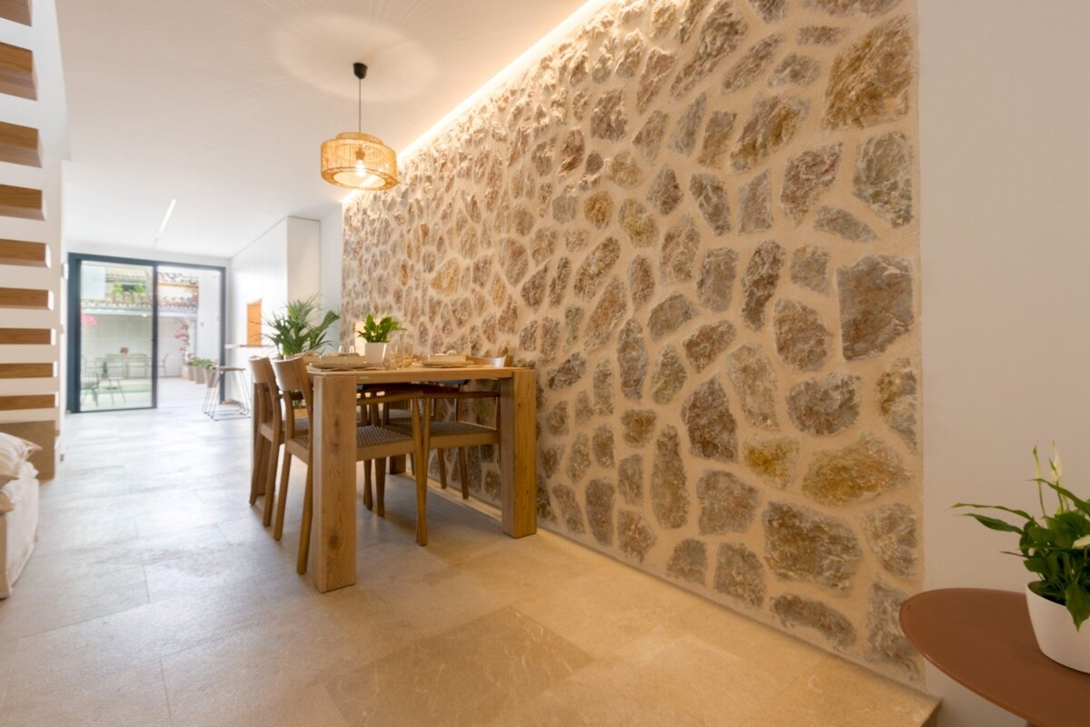 A modern dining area features a striking natural stone accent wall, a wooden table with woven chairs, and a pendant light. A glass door opens to an outdoor space.