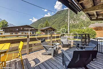 A balcony with chairs and a table with a mountain in the background