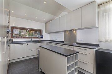 A modern kitchen with light grey cabinets, dark countertops & floor, an island, and a window showing a village amidst hills.