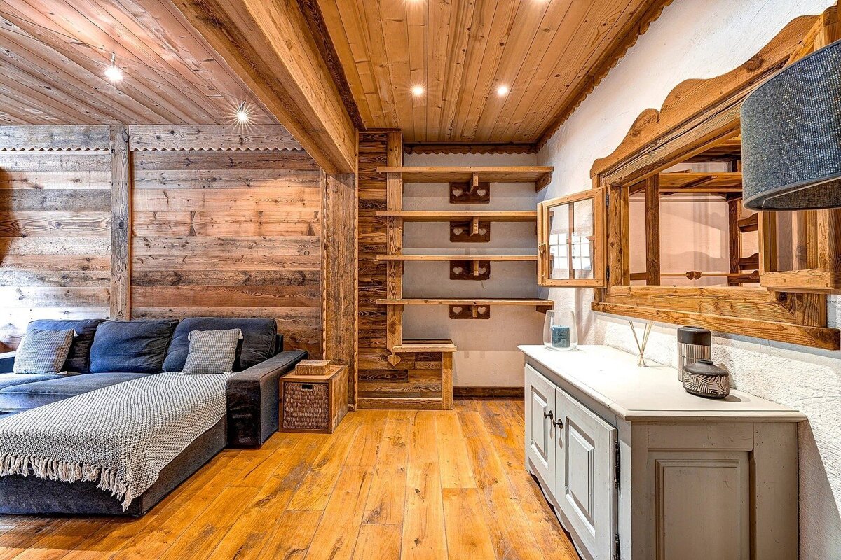 A cozy, wood-paneled room featuring a dark blue sofa, rustic shelves, and a light-colored cabinet, creating a warm chalet ambiance.
