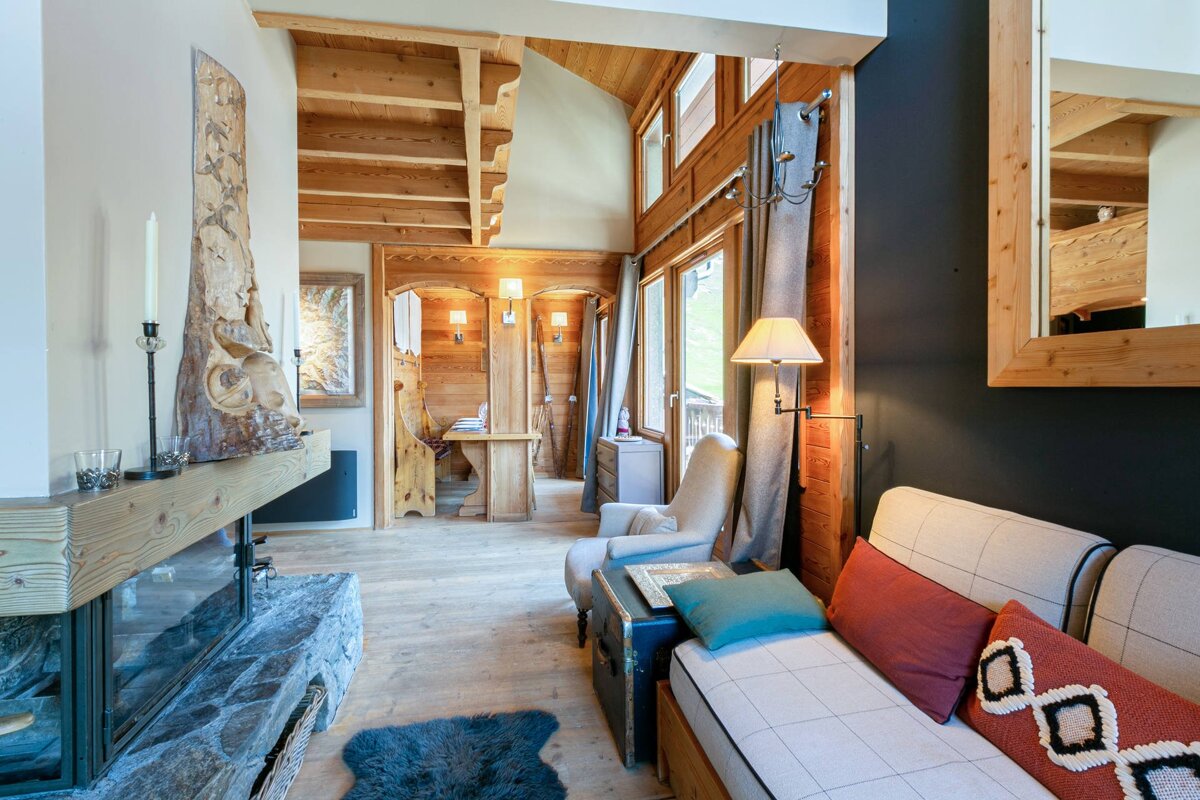 Cozy wooden chalet interior featuring a living area with a fireplace, comfortable seating, and rustic wood-paneled walls and ceiling.