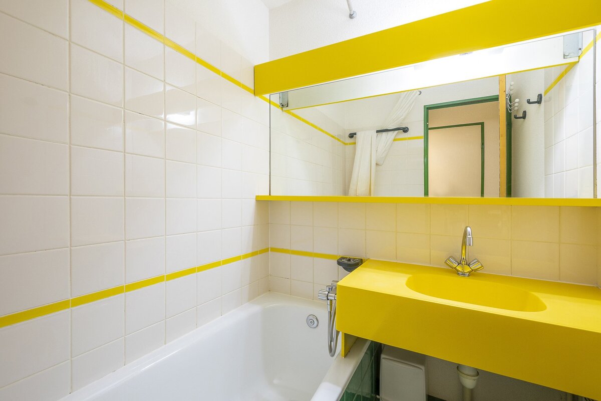 A bathroom with white tiles and a yellow sink