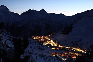 A snowy mountain valley with buildings lit up at night