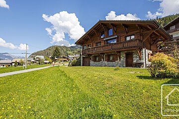 A large wooden house sits in the middle of a lush green field