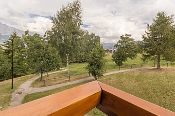 A wooden railing overlooking a grassy area with trees and a path