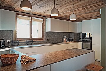 Modern kitchen with a rustic wooden ceiling, pendant lights, sleek white cabinetry, and stone-textured countertops.