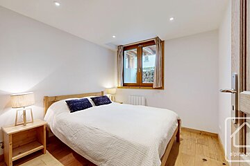 Cozy bedroom with white walls, wooden bed frame, white bedding, blue pillows, nightstands with lamps, and a wooden window with curtains.