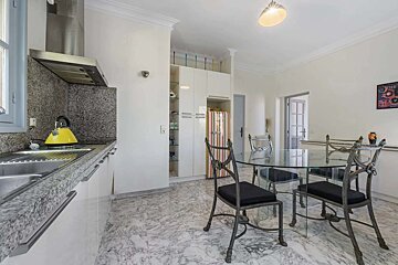 A bright kitchen and dining area features granite countertops, a yellow kettle, white cabinets, and a striped retro fridge, alongside a glass dining table with ornate metal chairs, all set on a marble