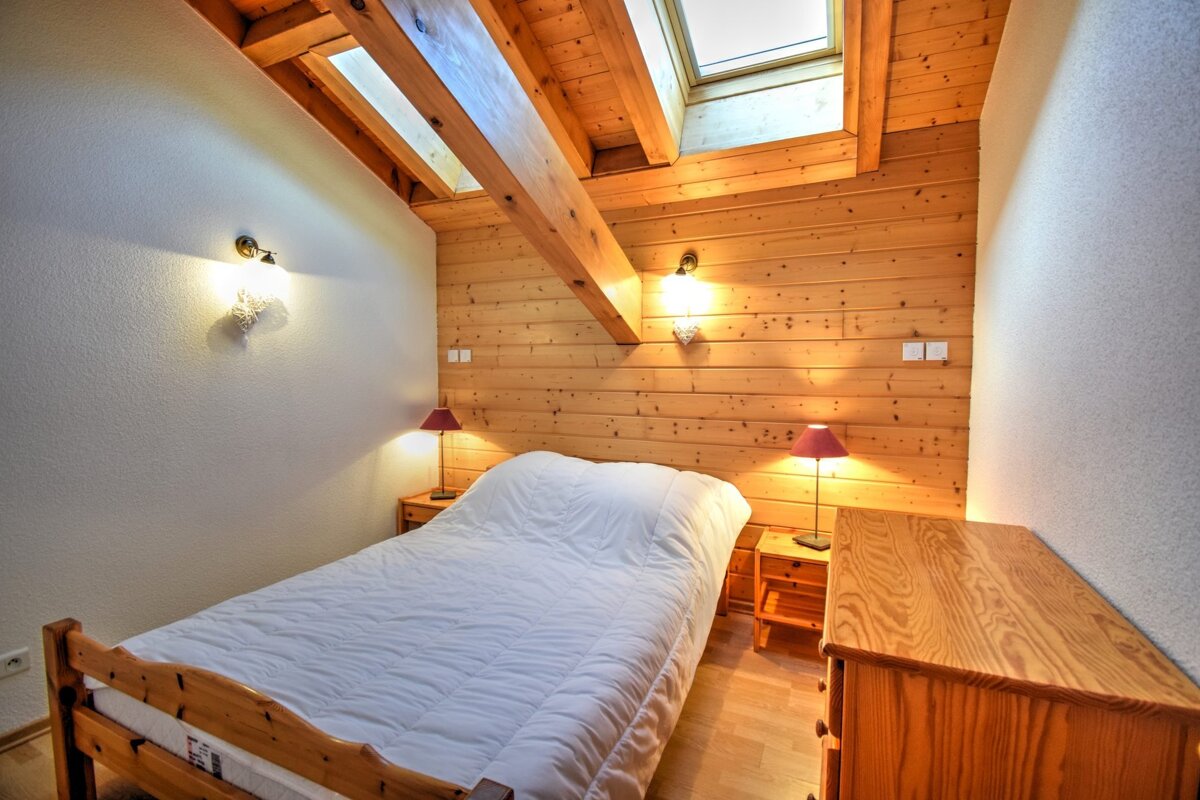 Cozy attic bedroom featuring wooden walls and ceiling, a slanted roof with skylights, a white bed, and warm lighting.