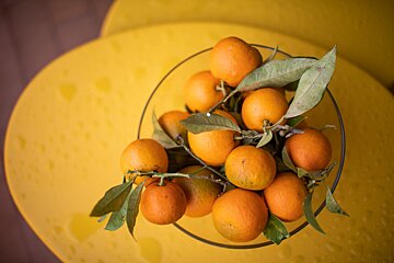 A bowl of oranges sits on a yellow table