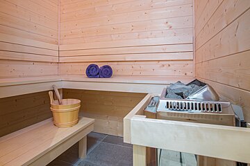 A wooden sauna with a bucket and towels on the shelf