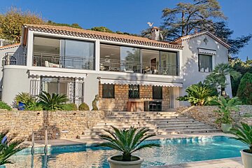 A luxurious two-story villa featuring a swimming pool, stone steps, and lush palm trees under a clear blue sky.