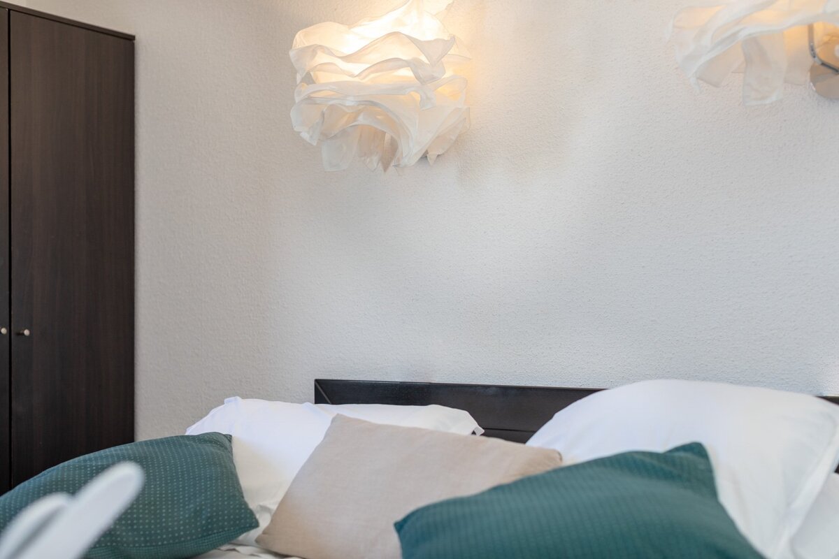 A bed with pillows and a lamp on the wall above it