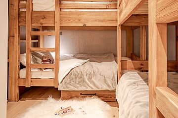 A cozy children's room featuring natural wood bunk beds with soft bedding, a teddy bear, and a fluffy white rug on a wooden floor.