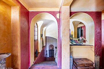 An ornate interior featuring colorful arched doorways in red and yellow plaster, overlooking a staircase.