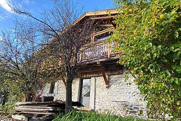 A stone house with a wooden balcony and a tree in front of it