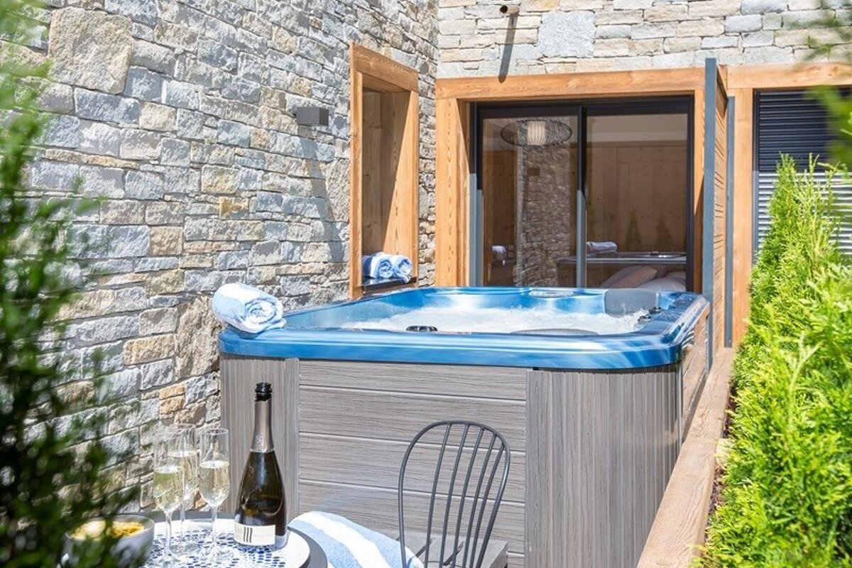 An outdoor hot tub set against a stone wall, with a bottle of champagne and glasses prepared on a nearby table.