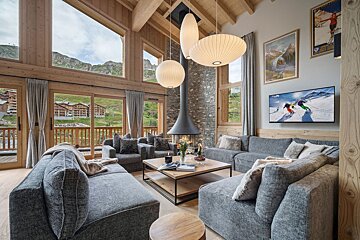 Luxurious ski chalet living room with mountain views, a modern fireplace, comfy grey sofas, and large windows.