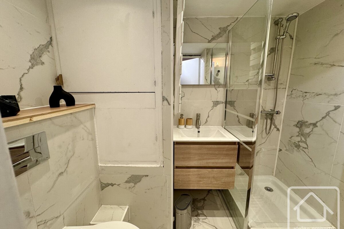 A modern bathroom featuring marble-patterned tiles, a wooden vanity with drawers, a sink, and a glass-enclosed shower.