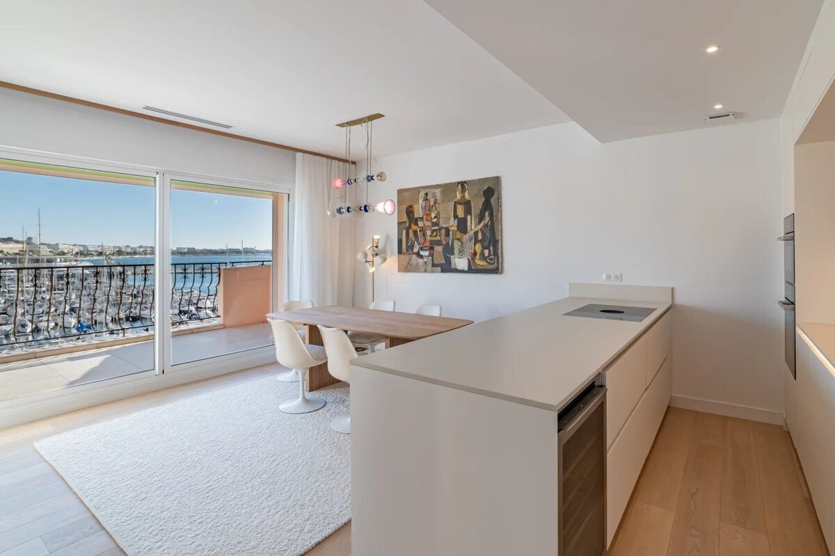 Bright, modern open-plan living space with dining area, kitchen, and a balcony offering expansive views of a marina.