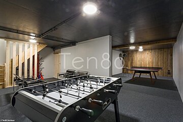 A game room with a foosball table and a ping pong table with ten80 written on the wall