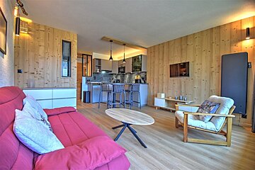 Cozy studio apartment with wood-paneled walls, a vibrant red sofa, a coffee table, and an open-plan kitchen in the background.