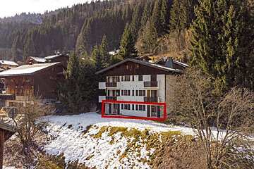 A building with a red circle around it is surrounded by snow and trees