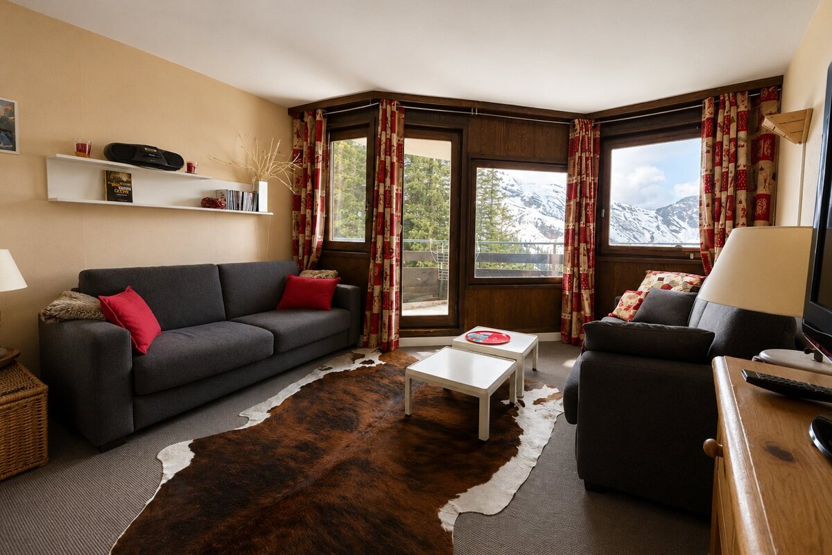 A cozy living room with grey sofas, a cowhide rug, and large windows showcasing snowy mountain views.