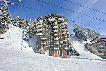 A ski lift going up a snow covered slope with a building in the background