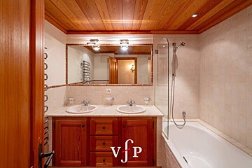 Warm bathroom with a wood-paneled ceiling, a double-sink vanity, and a bathtub with a glass screen.