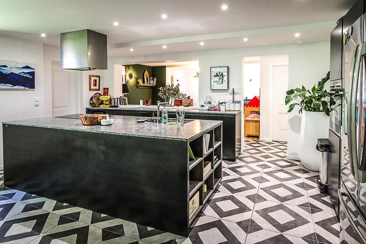 A modern kitchen features two dark islands with light countertops, a striking black and white geometric patterned floor, and an open-plan layout.