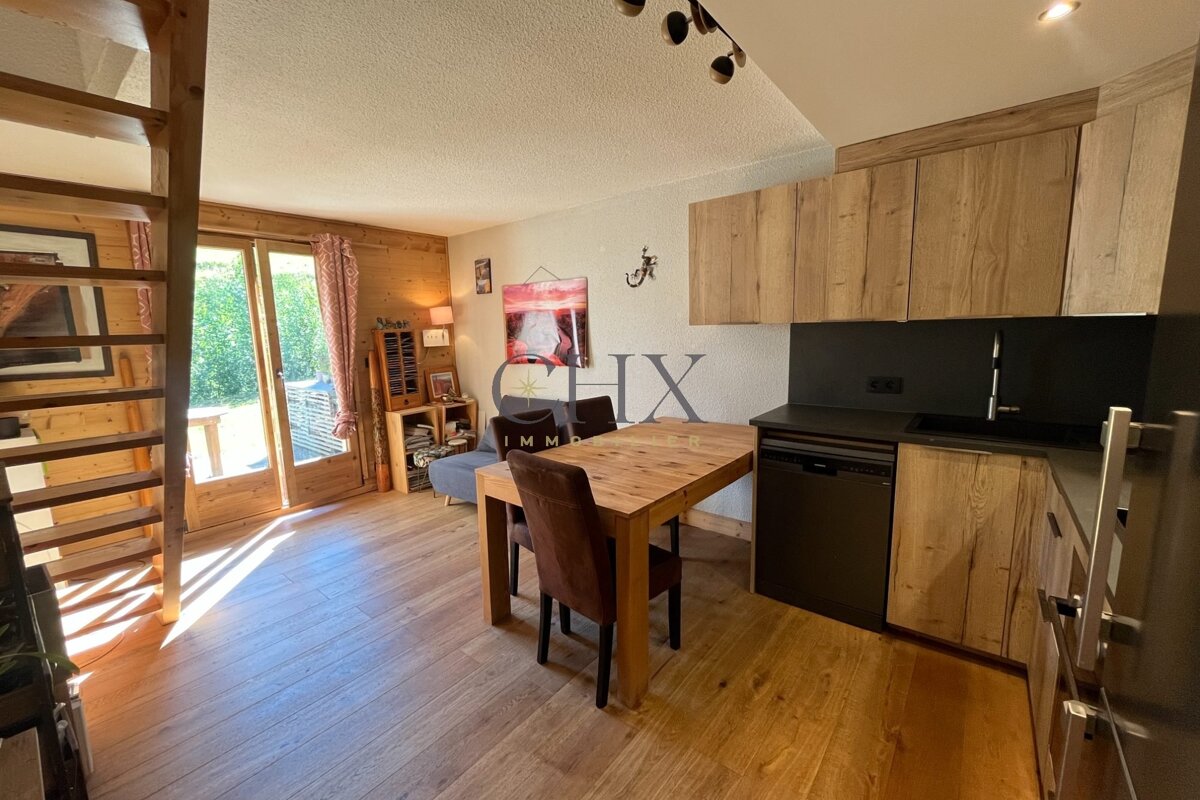Cozy cabin interior with a wooden kitchen, dining table, stairs, and glass doors leading to the outside.